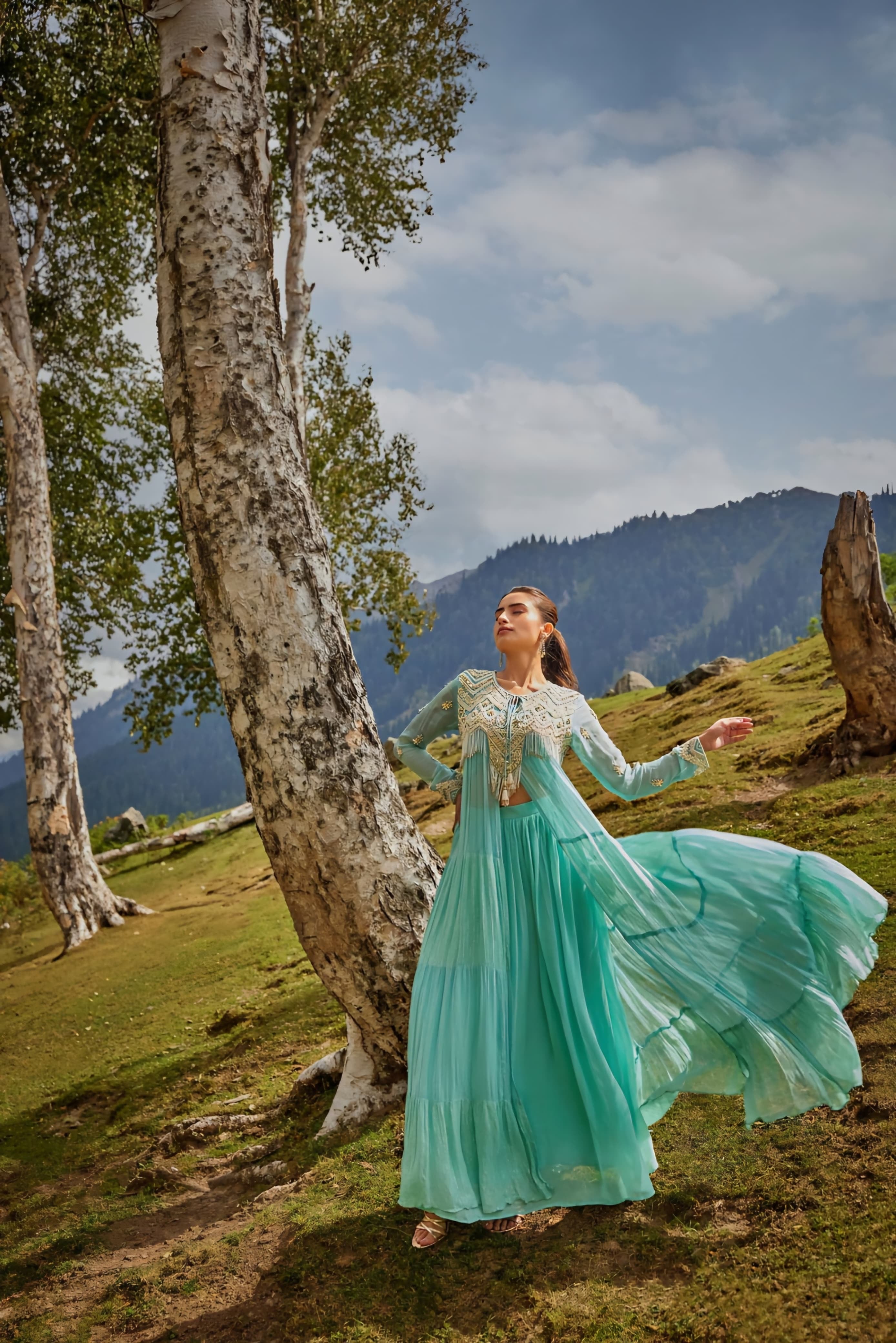 Aqua flowing embroidered Anarkali dress with sheer bodice and tiered flare in an outdoor setting.